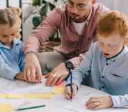 Teacher in eyeglasses helping preschoolers with drawing at table in classroom