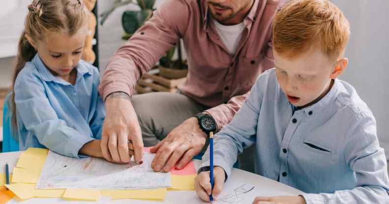 Teacher in eyeglasses helping preschoolers with drawing at table in classroom