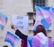 A protester wrapped in a trans Pride flag holds a 'Never Stop Fighting' placard during the trans rights demonstration