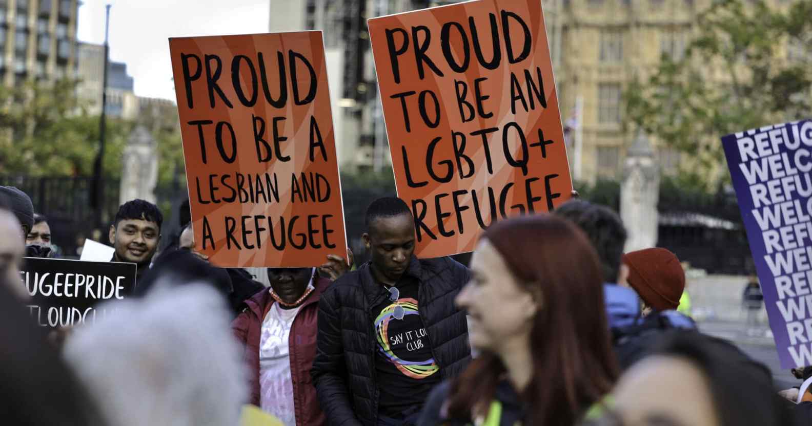 Protesters buttress placards up high standing in solidarity with queer refugees in Parliament Square