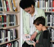 A person helps a child look at a book in a library setting