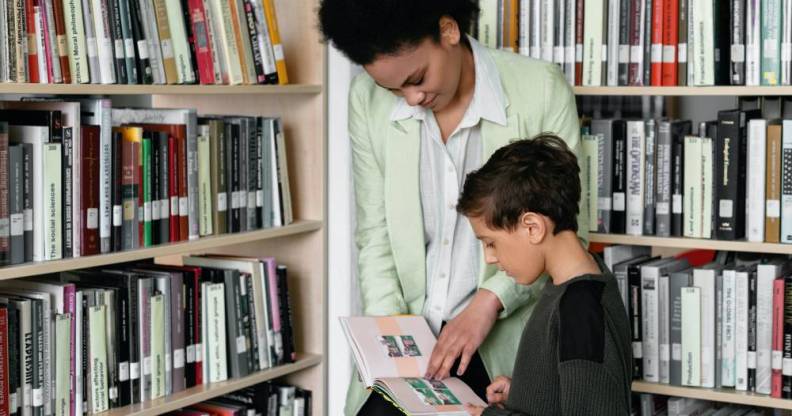 A person helps a child look at a book in a library setting