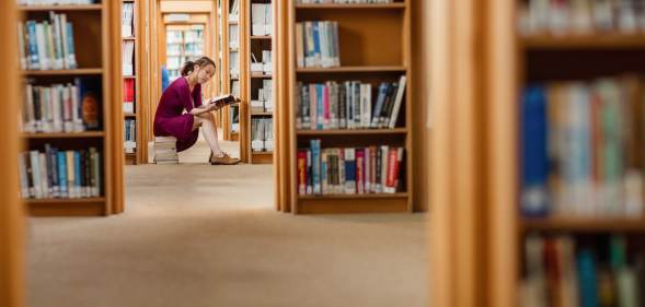 Young woman reading book in library at college