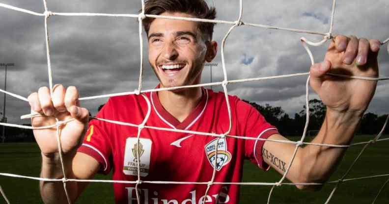 Adelaide United star Josh Cavallo poses in a football goal while wearing a red jersey