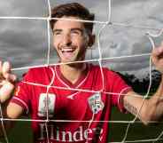 Adelaide United star Josh Cavallo poses in a football goal while wearing a red jersey