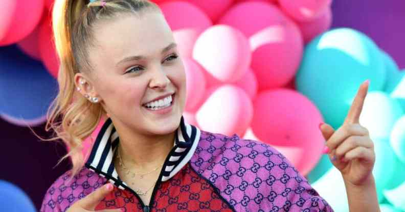 JoJo Siwa stands in front of colourful balloons while wearing red and purple jacket