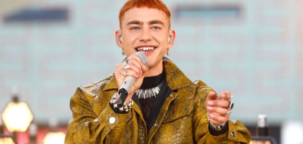 Olly Alexander in a yellow/green snakeskin jacket holding a microphone up to his mouth.
