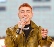 Olly Alexander in a yellow/green snakeskin jacket holding a microphone up to his mouth.