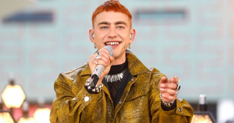 Olly Alexander in a yellow/green snakeskin jacket holding a microphone up to his mouth.