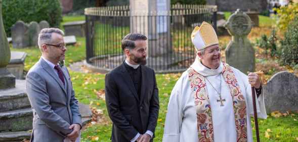 Male in grey suit and male in vicar's attire receive blessing from bishop