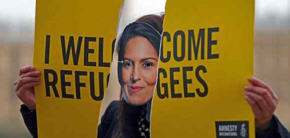 An activist from Amnesty International wears a mask depicting Britain's Home Secretary Priti Patel