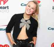 JoJo Siwa wears an open midriff-bearing black top with a silver bow and leather shorts