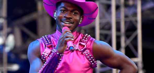 Lil Nas X performs in a hot pink outfit and matching cowboy hat holding a hot pink microphone