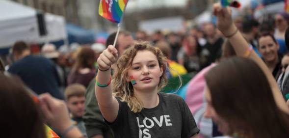 Young person holds up an LGBT+ pride flag while wearing a shirt that says 'love is love'