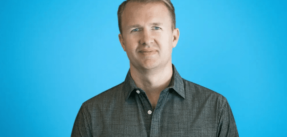 Jeff, wearing a dark grey shirt, smiling in front of a blue backdrop