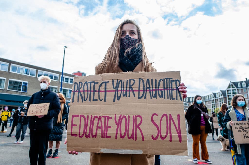 A woman holding a sign with 'protect your daughters' crossed out, and 'educate your son' written underneath