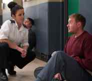Rose, a prison warden, crouching down to talk to Troy, who is sat on the floor, in Screwed