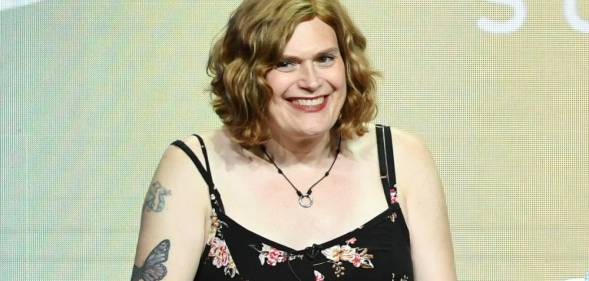 Lilly Wachowski wears a black patterned dress and sits in front of a grey-green background