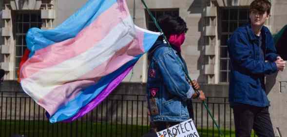 A protester holds a trans pride flag and a placard that reads "Protect Trans Kids" placard during the trans rights demonstration