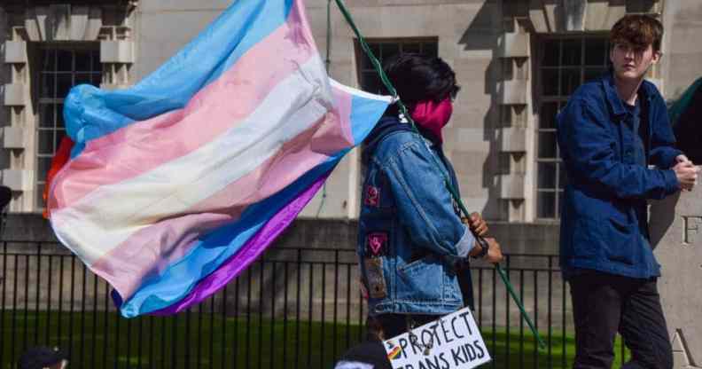 A protester holds a trans pride flag and a placard that reads "Protect Trans Kids" placard during the trans rights demonstration