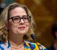 Kyrsten Sinema wears a black, blue, yellow and white patterned top while speaking into a microphone at a US Senate Committee on Finance hearing