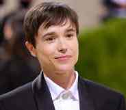 Elliot Page smiles at the camera while wearing a white button up shirt and black suite jacket