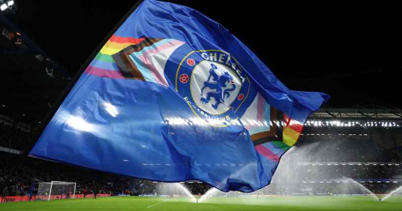 A flag bearer waves a Chelsea FC flag with the LGBT+ Progress flag design
