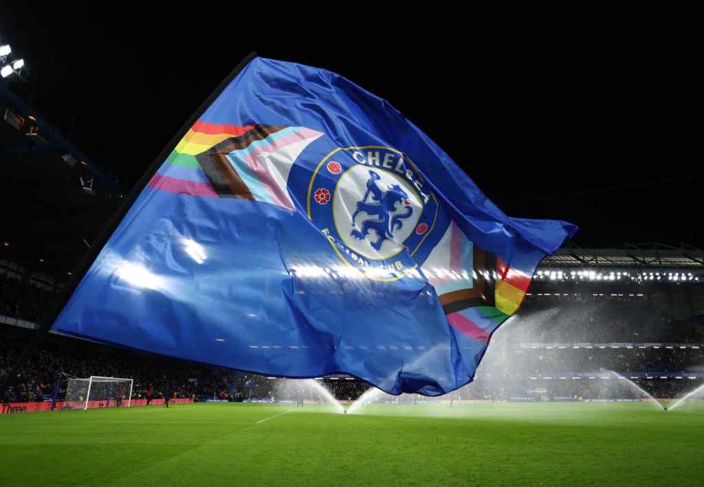 A flag bearer waves a Chelsea FC flag with the LGBT+ Progress flag design