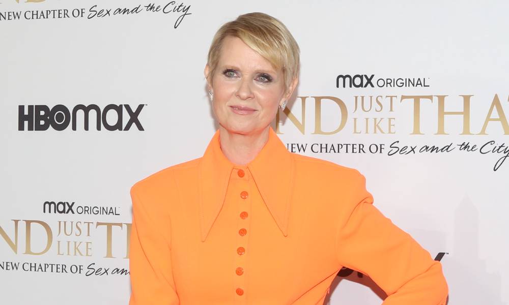 Cynthia Nixon wears an orange outfit and smiles at the camera