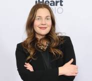 Drew Barrymore crosses her arms and smiles at the camera while wearing a black coloured outfit