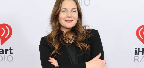 Drew Barrymore crosses her arms and smiles at the camera while wearing a black coloured outfit