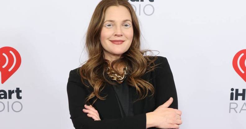 Drew Barrymore crosses her arms and smiles at the camera while wearing a black coloured outfit
