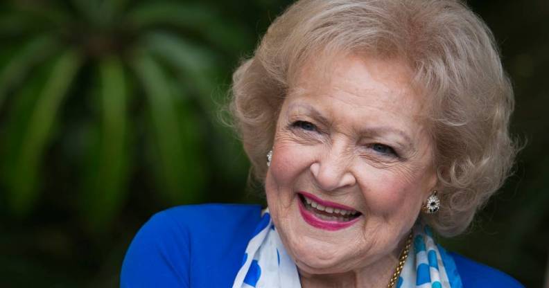 Betty White smiles at the camera while wearing a blue jacket and blue and white scarf