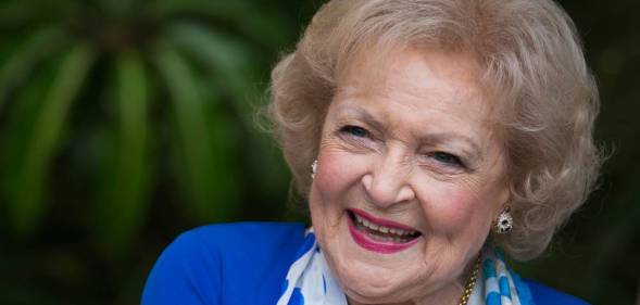 Betty White smiles at the camera while wearing a blue jacket and blue and white scarf