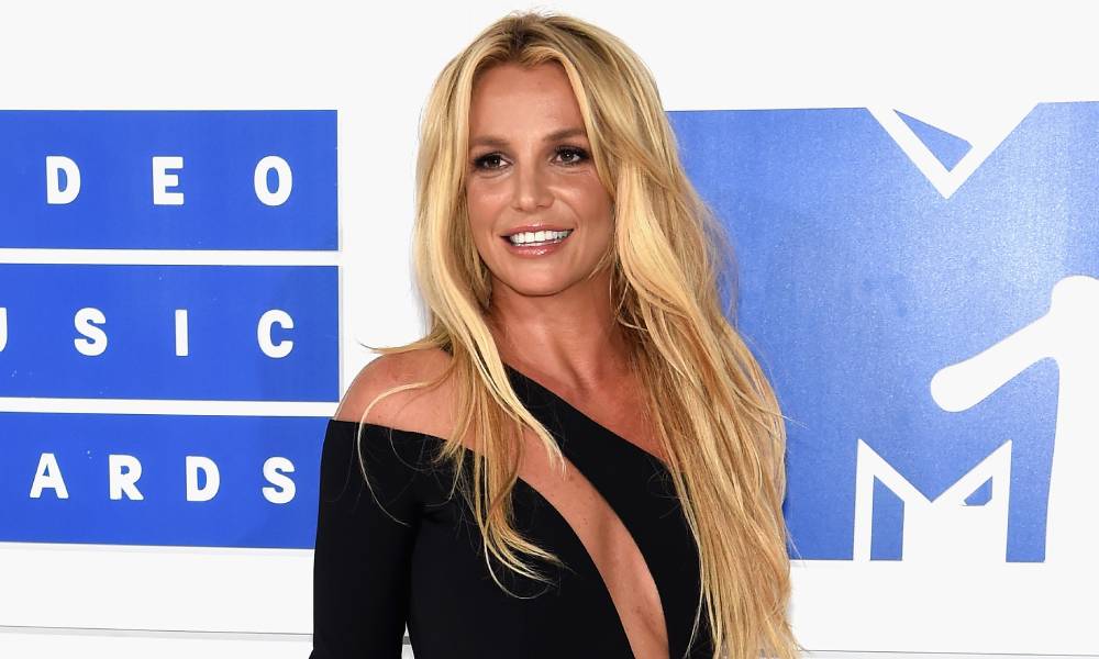 Britney Spears appears in a black dress with cut outs amid a blue and white background