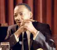 Martin Luther King Jr sits at a table with his hands folded in front of his face