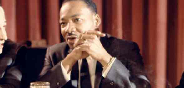 Martin Luther King Jr sits at a table with his hands folded in front of his face