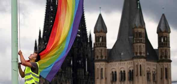The Cologne Cathedral (L) and the church Gross St Martin (R) are seen in the background as a man hoists a rainbow flag