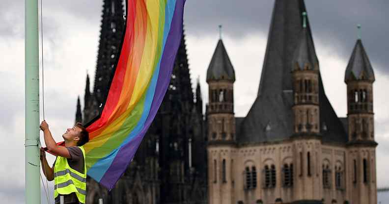 The Cologne Cathedral (L) and the church Gross St Martin (R) are seen in the background as a man hoists a rainbow flag