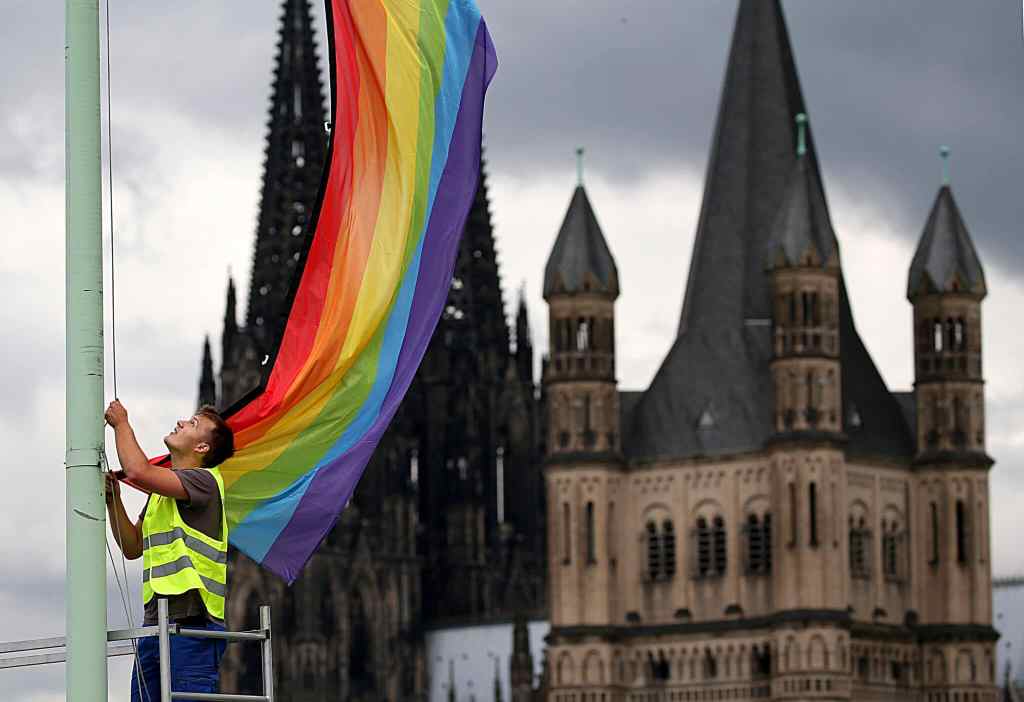 The Cologne Cathedral (L) and the church Gross St Martin (R) are seen in the background as a man hoists a rainbow flag