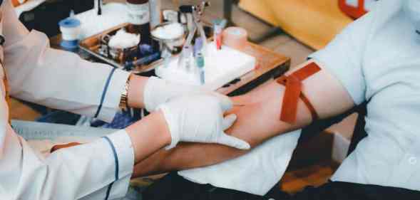A medical professional uses a needle to try to draw blood from a person sitting in a chair wearing a light blue shirt