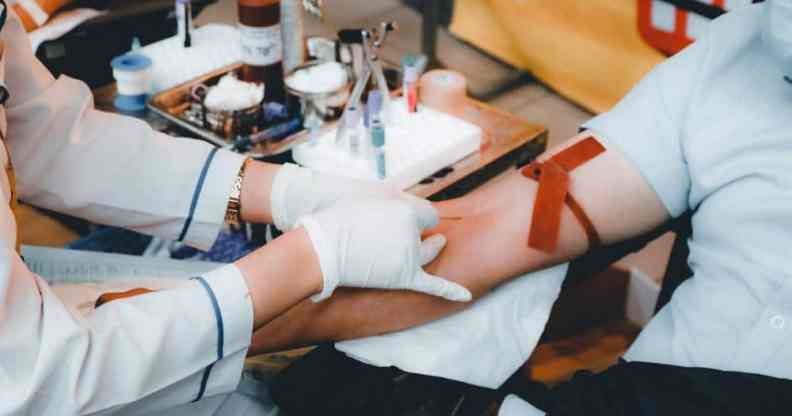A medical professional uses a needle to try to draw blood from a person sitting in a chair wearing a light blue shirt