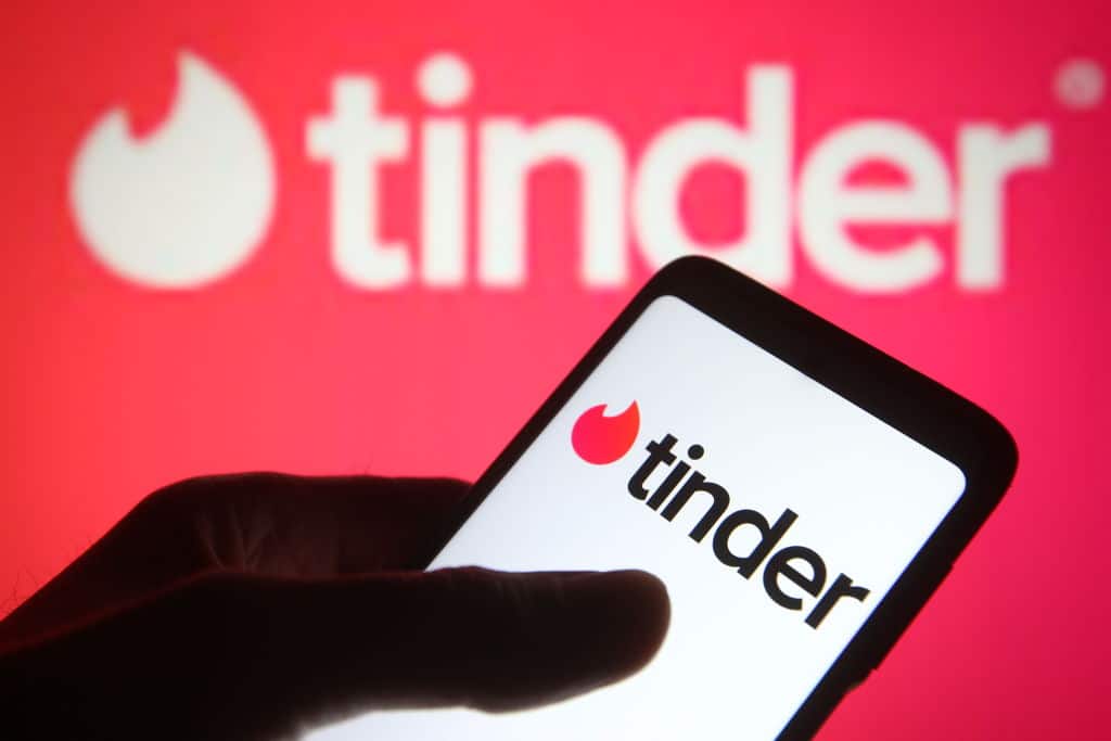 A phone with the Tinder logo, in front of another Tinder logo