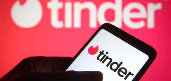 A phone with the Tinder logo, in front of another Tinder logo