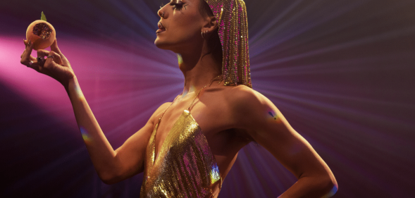 A performer in a gold headpiece holding a peach