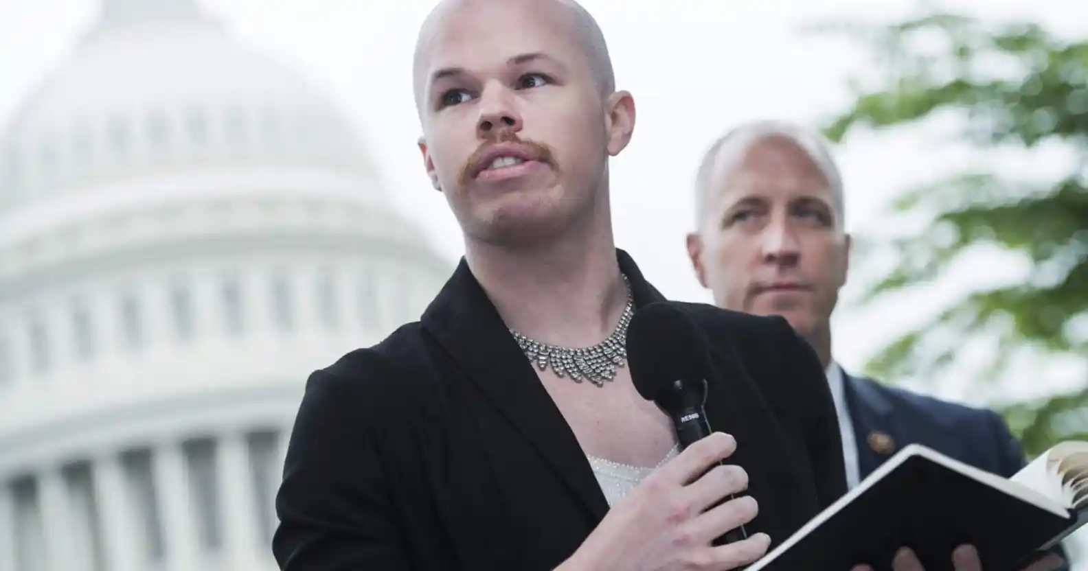 Sam Brinton wearing a woman's suit jacket with necklace speaks outside the US capitol
