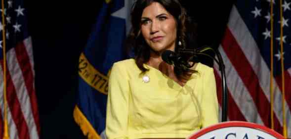 Kristi Noem, the governor of South Dakota, is wearing a yellow outfit while standing at a podium