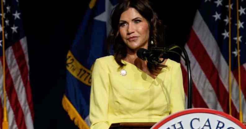 Kristi Noem, the governor of South Dakota, is wearing a yellow outfit while standing at a podium