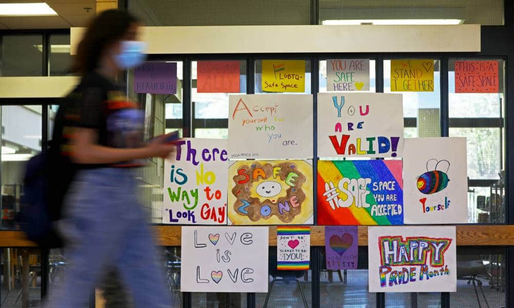 Several LGBT+ posters celebrating Pride month are posted on a glass partition in a high school