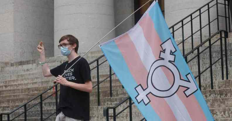 A protester holds the trans flag and snaps in solidarity with other speakers, during a trans rights demonstration